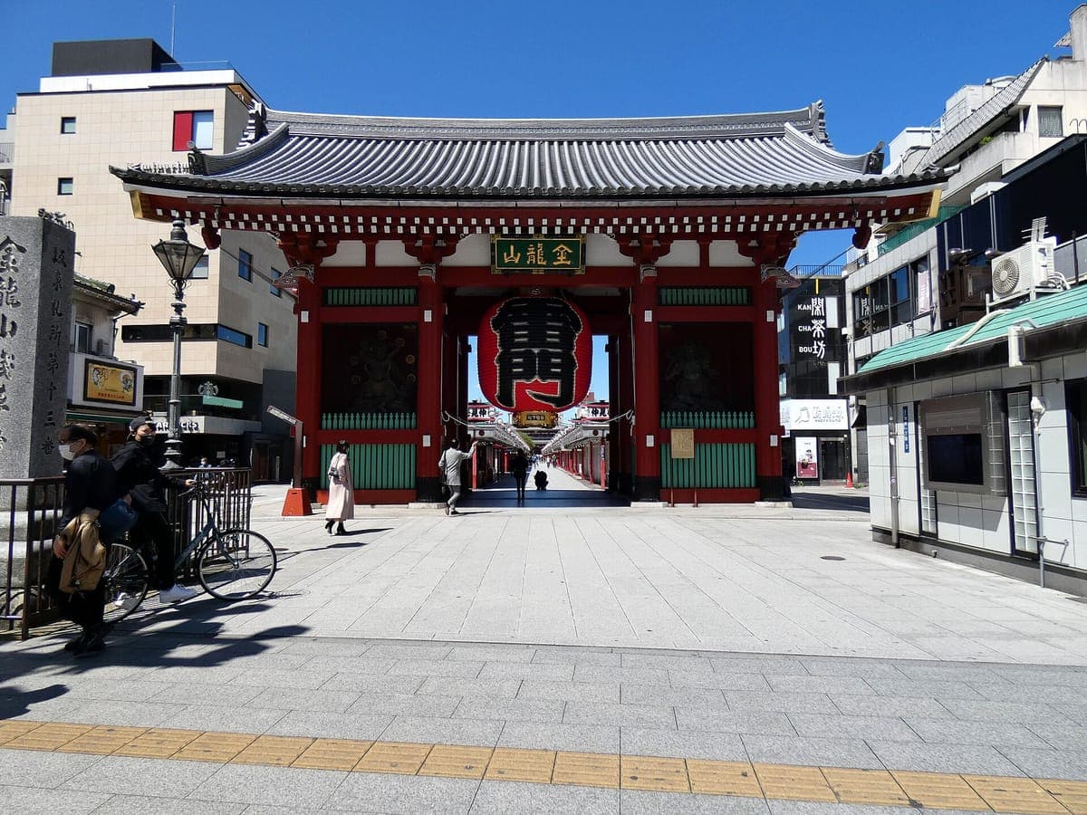 O portão vermelho Kaminarimon de Sensō-ji com sua lanterna vermelha gigante marcada 雷門, visto através de uma praça de pedra quase vazia