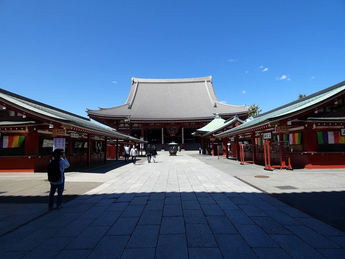 O salão principal de Sensō-ji com seu grande telhado de telhas cinza no final de uma ampla entrada de pedra sob um céu azul claro