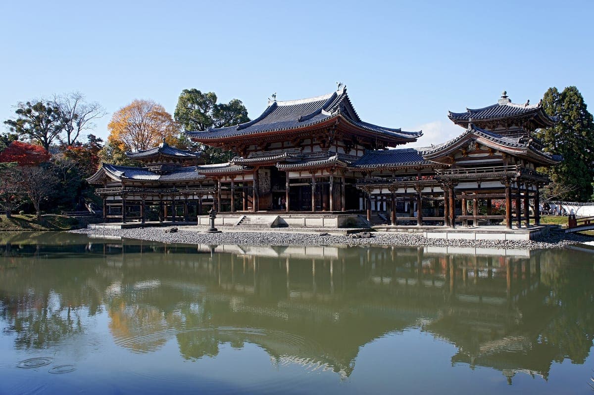 O Phoenix Hall vermelho de Byōdō-in com seu salão central e duas alas, refletido em um lago calmo sob um céu azul claro