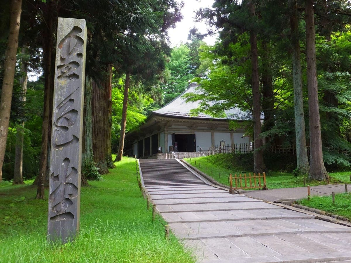 Uzun sedir ağaçlarının arasından Chūson-ji'deki Konjikidō'ın alçak koruyucu salonuna giden taş yolun yanında altın salonun adının yazılı olduğu uzun bir ahşap direk