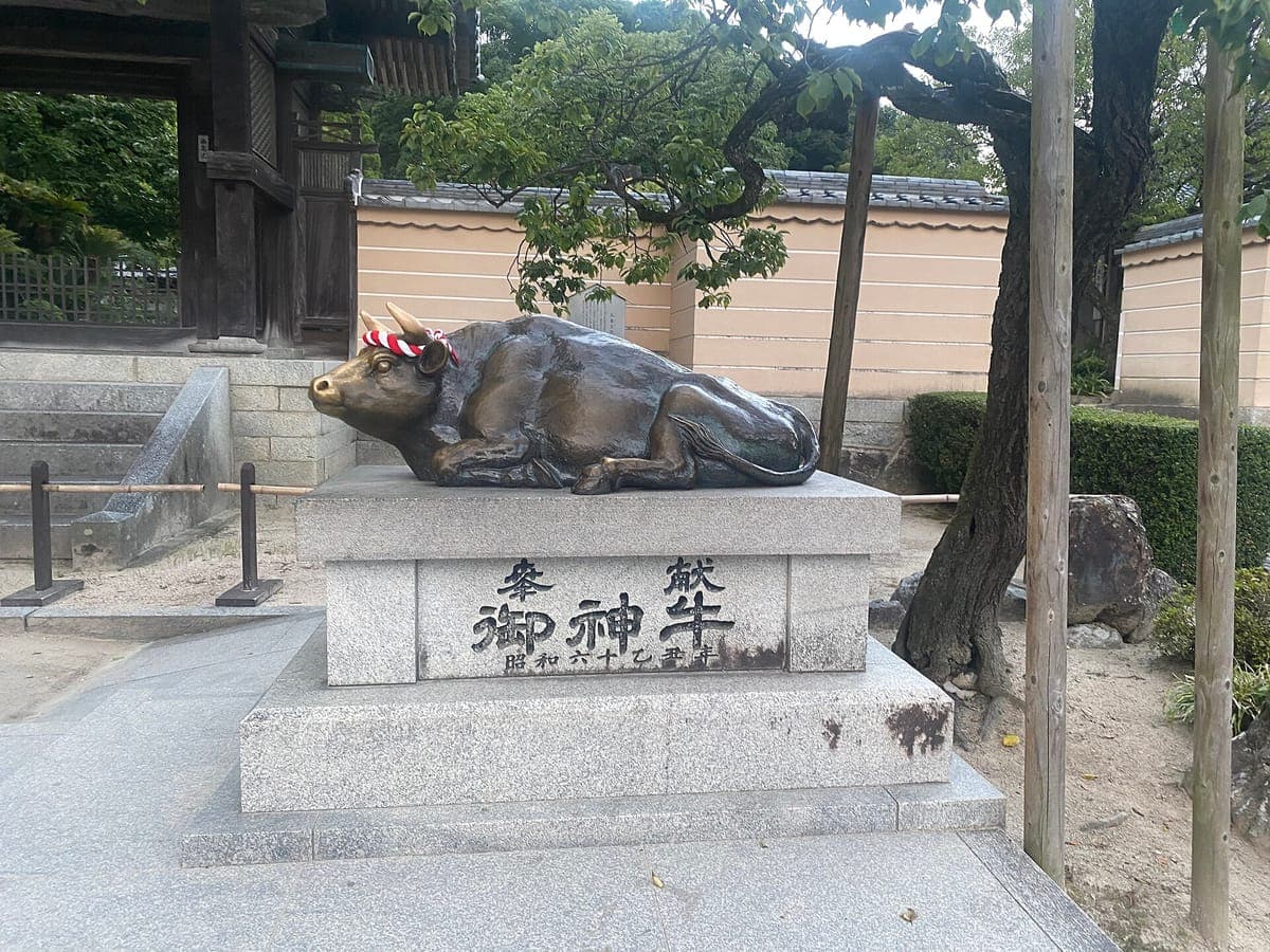 Eine liegende bronzene Stierstatue auf einem Steinsockel mit der Inschrift goshingyū bei Dazaifu Tenmangū, deren Kopf durch Berührung poliert wurde