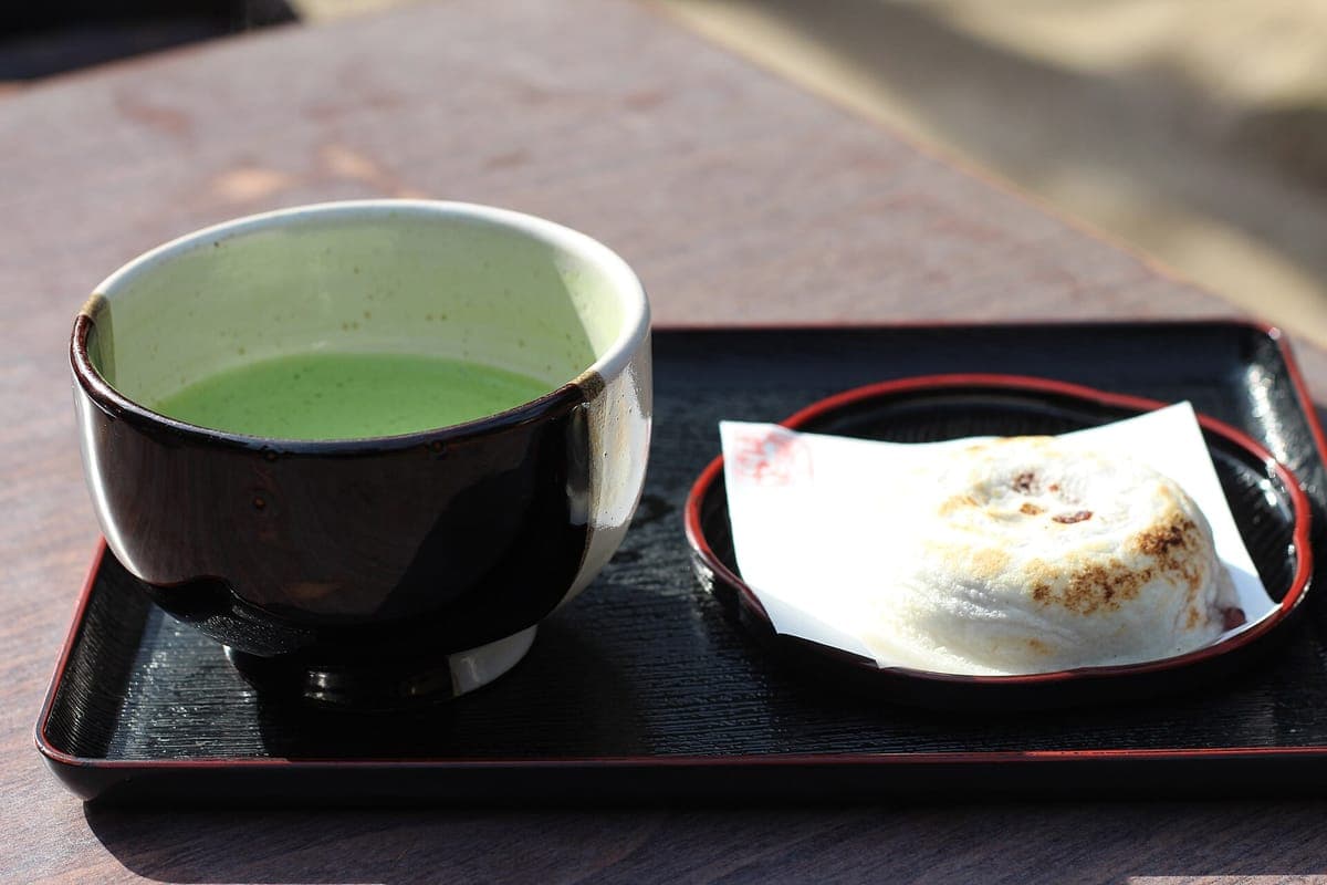 Ein Lacktablett mit einer Schüssel mit geschlagenem grünem Matcha und einem gegrillten umegae mochi Reiskuchen auf weißem Papier