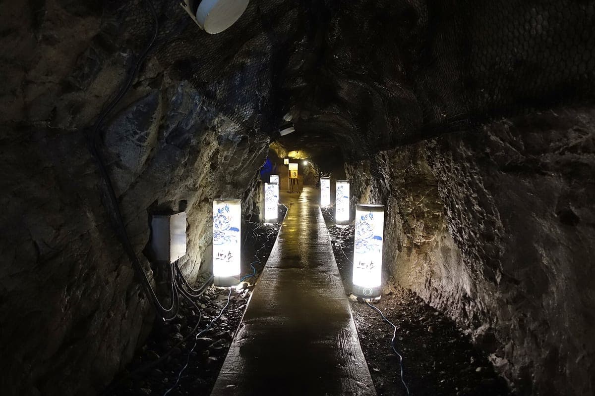 Úzký chodník vedoucí do temného skalního tunelu v Iwaya jeskyních na Enošimě, lemovaný zářícími papírovými lucernami
