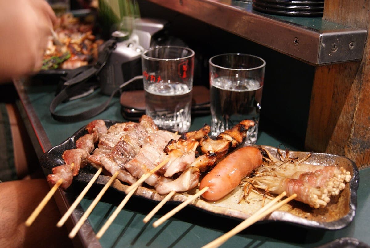 จานเนื้อย่างและผักเสียบไม้พร้อมไส้กรอกบนเคาน์เตอร์ yatai ข้างน้ำสองแก้ว