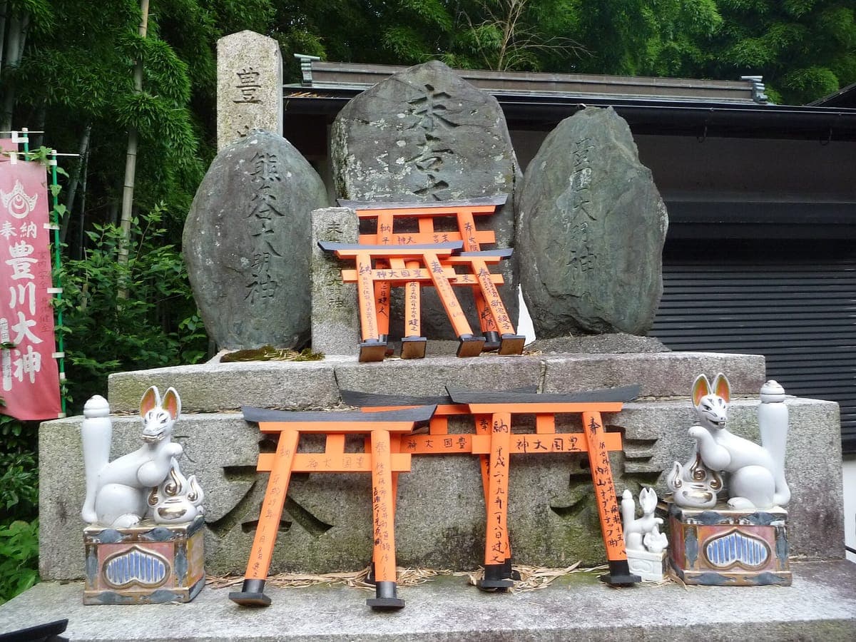 Un par de estatuas de zorros blancos junto a pequeñas ofrendas de torii bermellones y piedras con inscripciones en Fushimi Inari Taisha