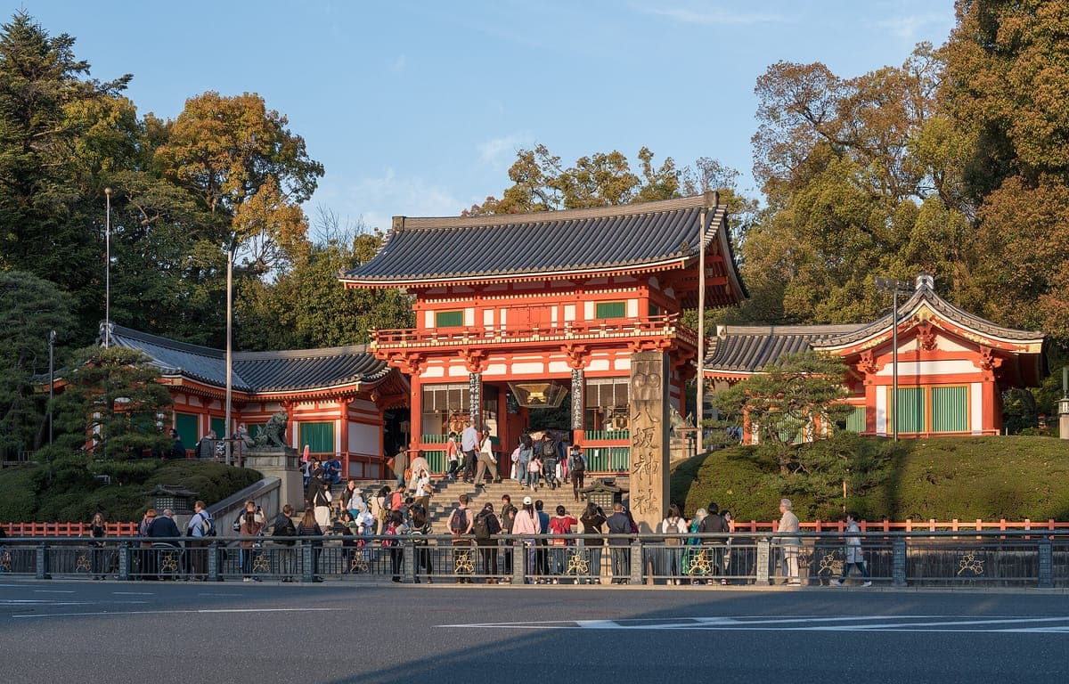 Rumělková dvoupatrová Nishirōmon věžová brána Yasaka Jinja na vrcholu kamenných schodů, obrácená ke konci Shijō-dōri, se stromy vzadu
