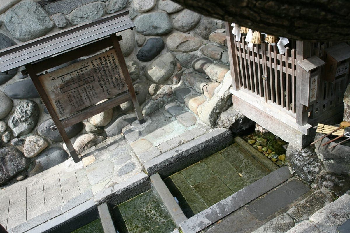 Les bassins en pierre de la source Sōgisui à Gujō Hachiman, avec de l'eau claire coulant entre eux, un petit sanctuaire en bois et un panneau explicatif