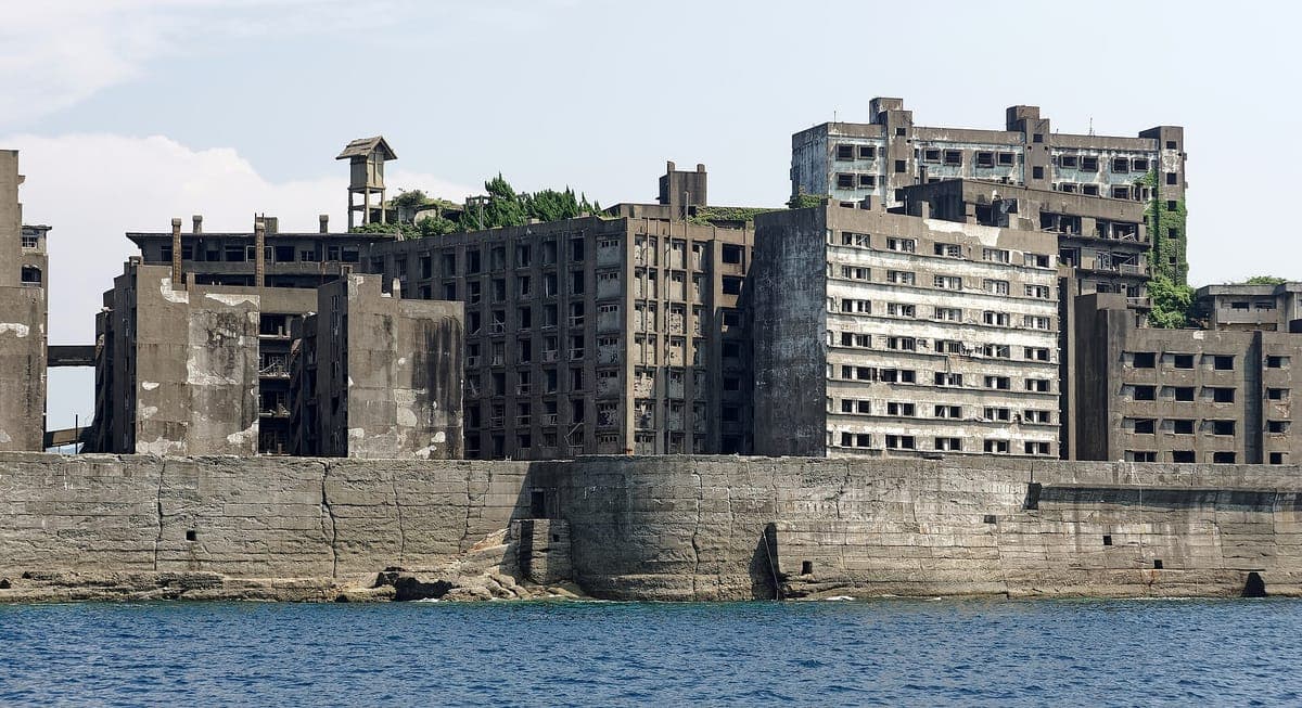 Hashima'ın beton deniz duvarının ve onun arkasındaki çökmekte olan çok katlı apartman ve maden binalarının yakından görünümü