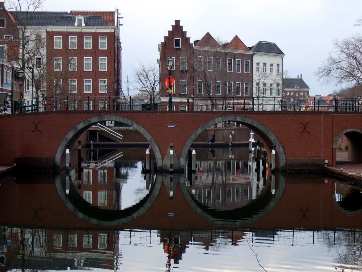 Isang brick bridge na may mga bilog na arko sa ibabaw ng still canal sa Huis Ten Bosch, na may matataas na Dutch-style brick na bahay na makikita sa tubig