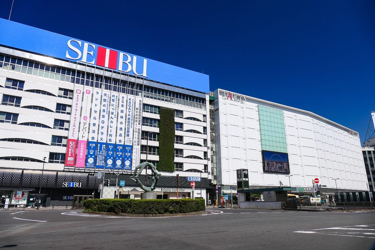 Ikebukuron aseman itäinen uloskäynti syvän sinisen taivaan alla, suuri Seibu rakennus ja sen kyltti tyhjää aukiota kohti