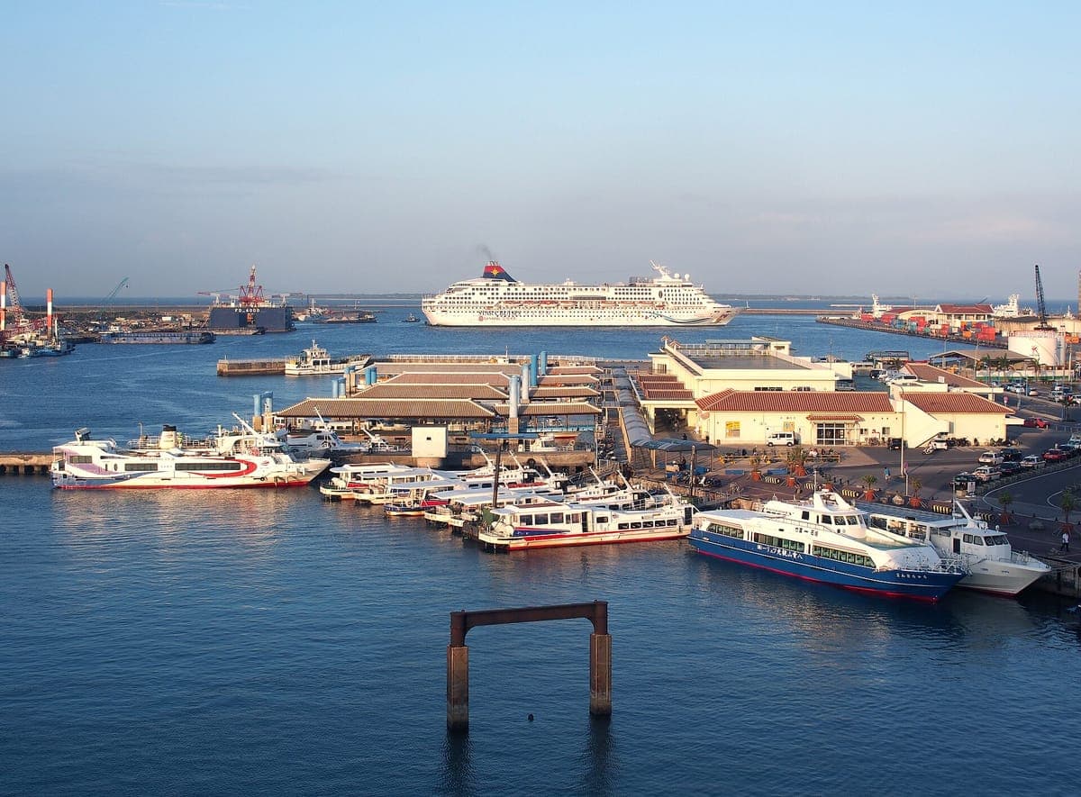 Der Hafen von Ishigaki von oben gesehen, mit weißen Hochgeschwindigkeitsfähren, die am abgelegenen Inselterminal festmachen, und einem Kreuzfahrtschiff in der Ferne