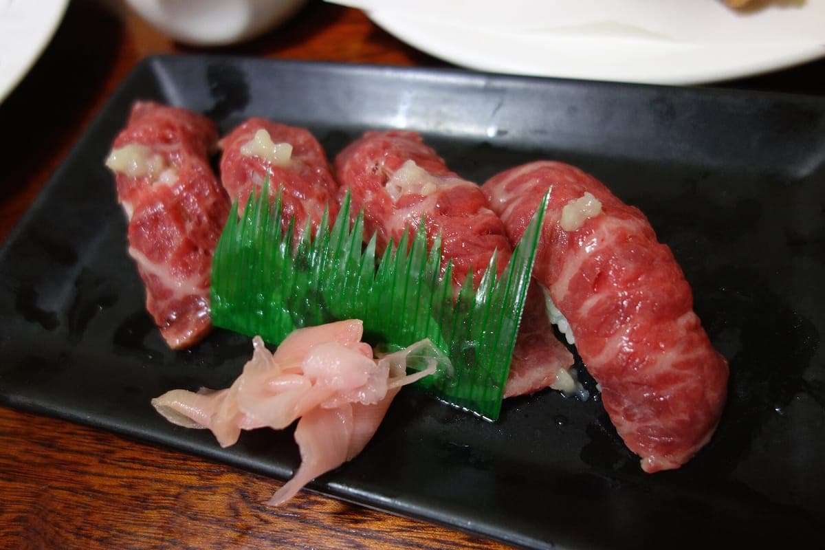 Vier Stücke Nigiri-Sushi, garniert mit marmoriertem rohem Ishigaki-Rindfleisch auf einem dunklen Teller mit eingelegtem Ingwer