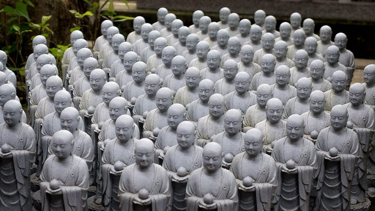 Řady malých šedých kamenných soch Jizō se zaoblenými hlavami a sepjatýma rukama na Hase-dera v Kamakura