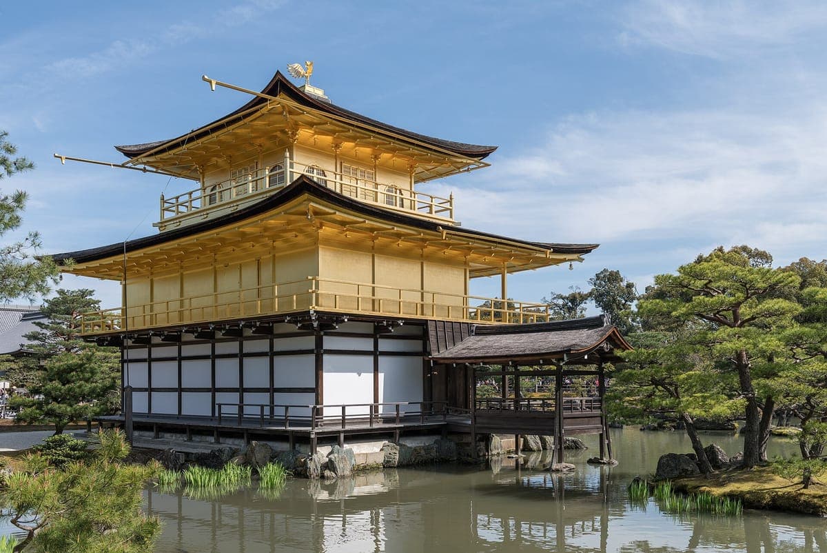 Malapit na tanaw ang Kinkaku-ji Shariden mula sa hilaga, na nagpapakita ng mga ginintuan na itaas na palapag, ang puting-paderang ground floor, ang gintong phoenix sa bubong at mga pine tree sa tabi ng tubig