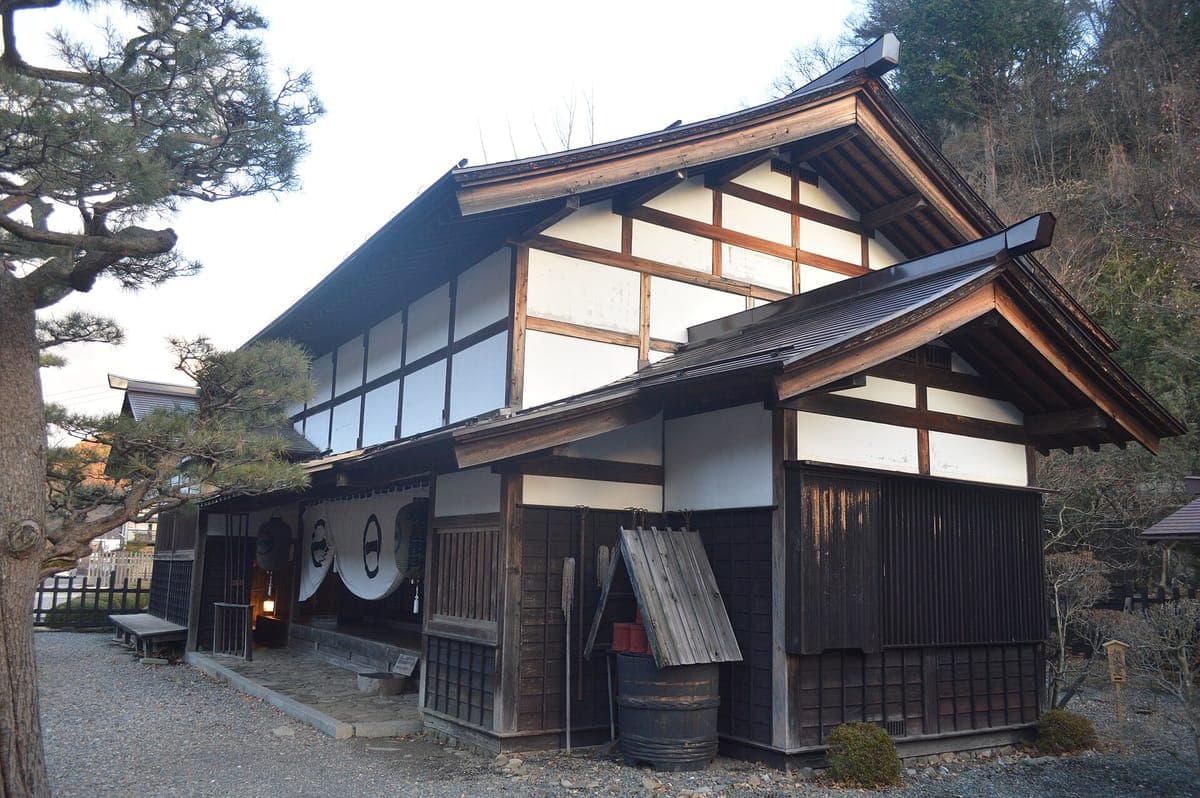 Zrekonstruovaná dřevěná budova Fukushima Checkpoint Museum v Kiso-Fukushima s bílými omítkovými stěnami, tmavými trámy, taškovou střechou a borovicí v přední části