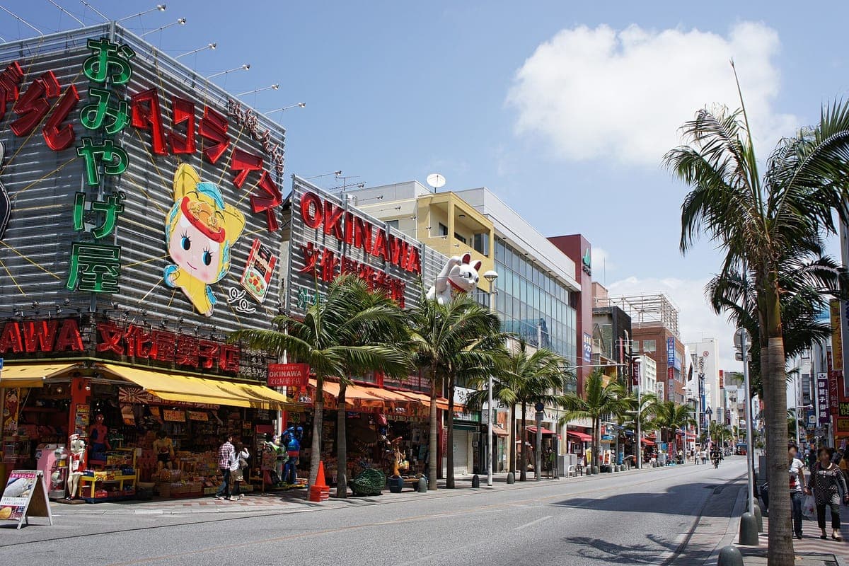 Kokusai-dōri in Naha an einem sonnigen Tag, mit Palmen auf dem Bürgersteig und bunten Souvenirladenschildern entlang der Straße