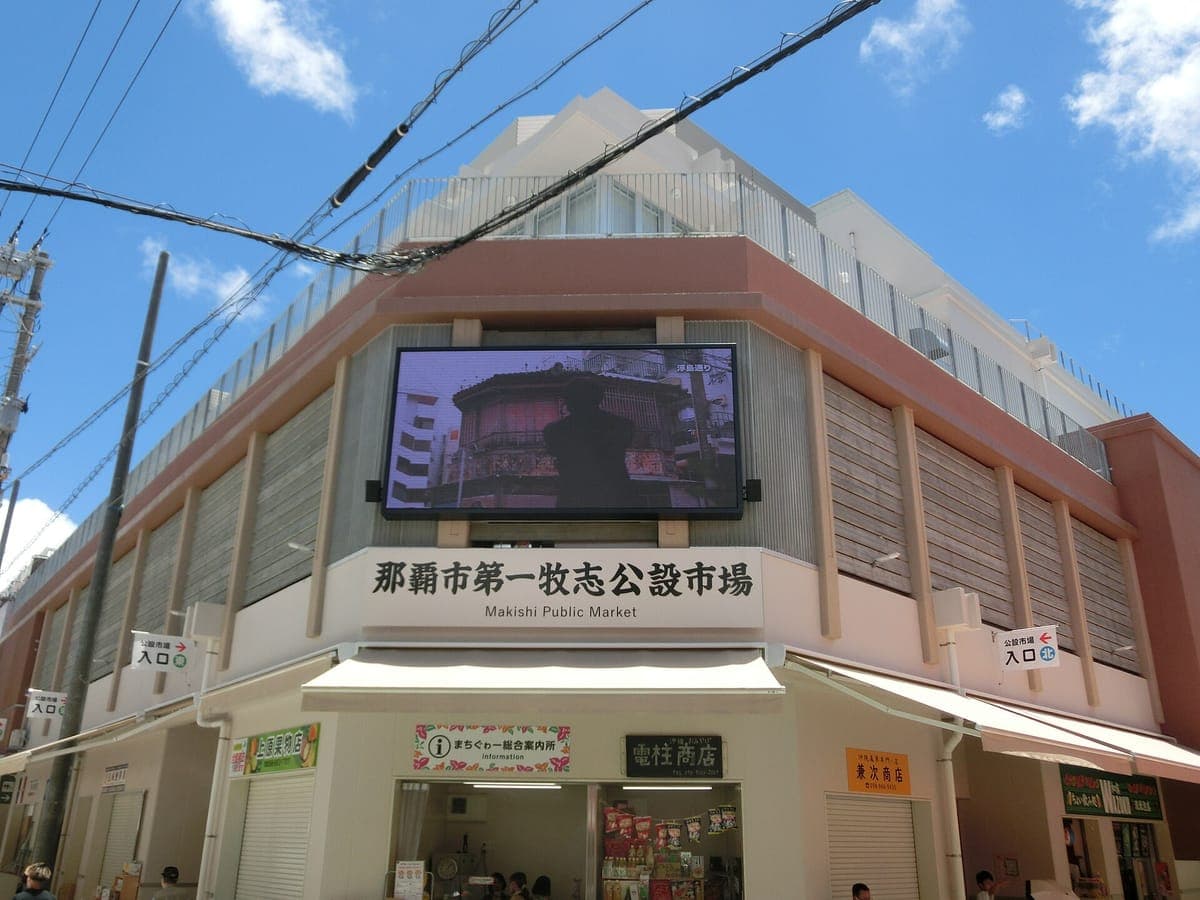 Das neue Gebäude des Naha City First Makishi Public Market mit seinem japanischen Namen an der Fassade und den Ladeneingängen auf Straßenniveau