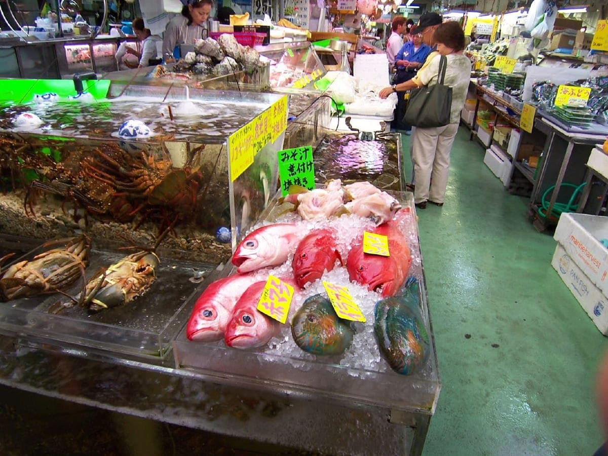 Ein Fischstand auf dem Makishi Public Market mit leuchtend roten und blauen Rifffischen und Krabben auf Eis unter handgeschriebenen Preisschildern