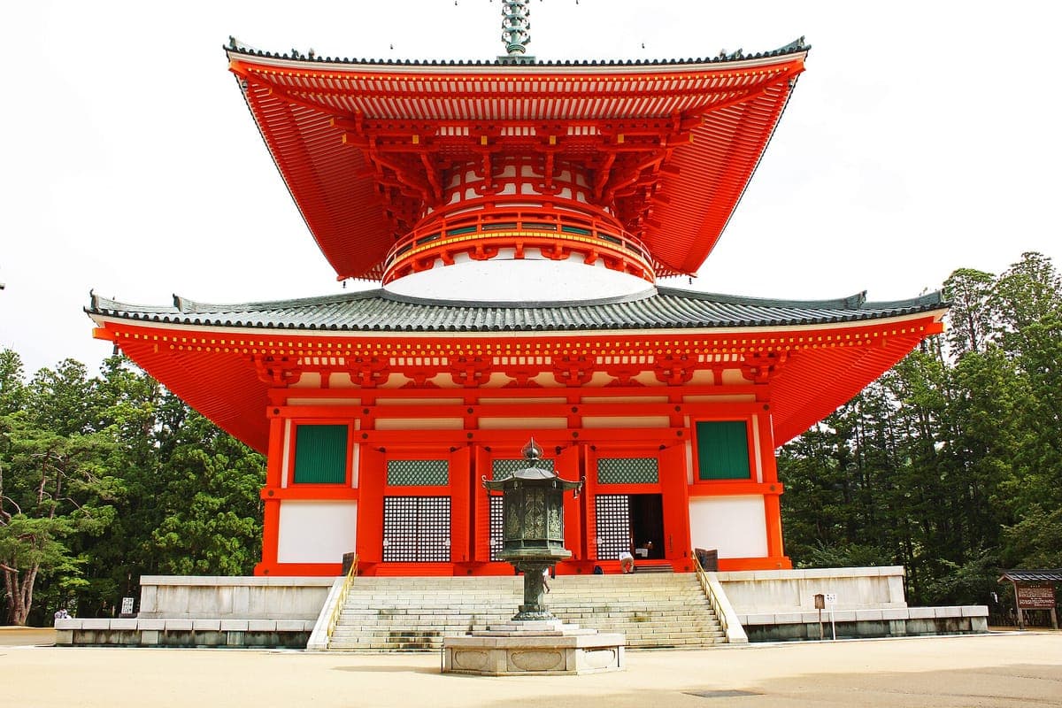 Яркая двухъярусная Konpon Daitō пагода на Danjō Garan на Kōyasan с бронзовым фонарем спереди и кедрами позади.