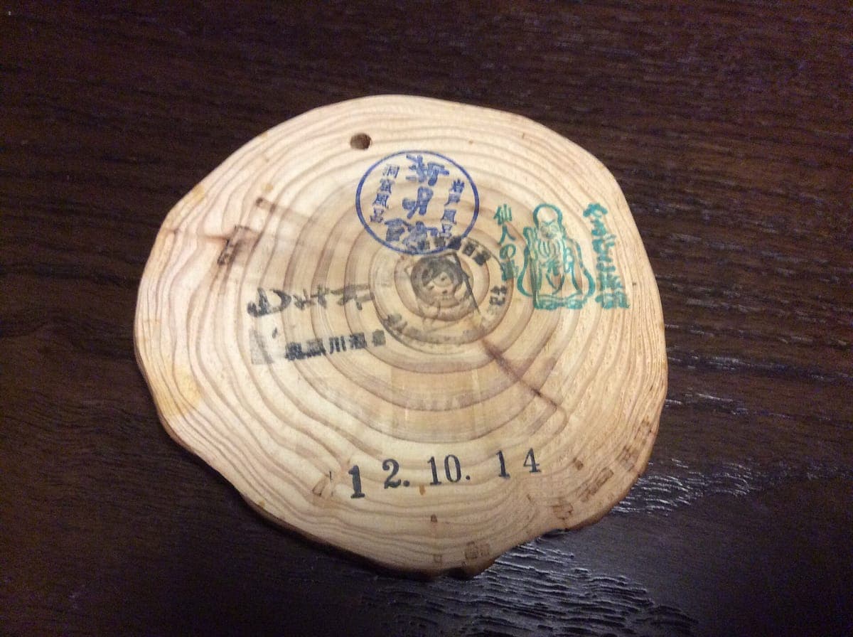 Isang bilog na hiwa ng kahoy na ginamit bilang Kurokawa Onsen bath pass, na nakatatak ng mga ink seal mula sa ryokan at petsa