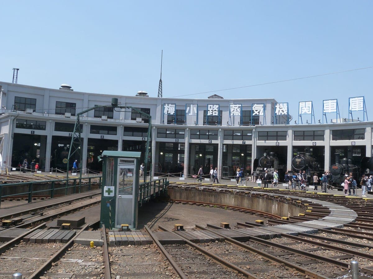 La rotonda curva de hormigón del Museo del Ferrocarril de Kioto con vías que parten de una gran plataforma giratoria en primer plano y una pequeña caseta de control verde