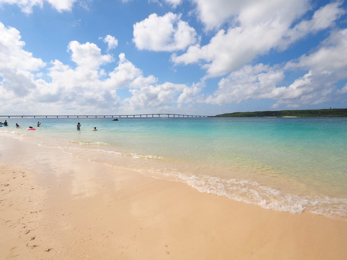 Weißer Sand und sehr klares türkisfarbenes Wasser am Yonaha Maehama Strand auf der Insel Miyako, mit einer langen, niedrigen Brücke am Horizont