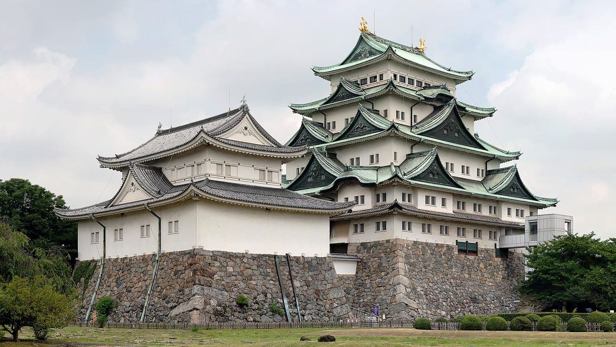 Der weiß-grün gedeckte Hauptfried der Burg Nagoya mit goldenem Shachihoko auf der Spitze und einem kleineren Bergfried daneben auf massiven Steinmauern