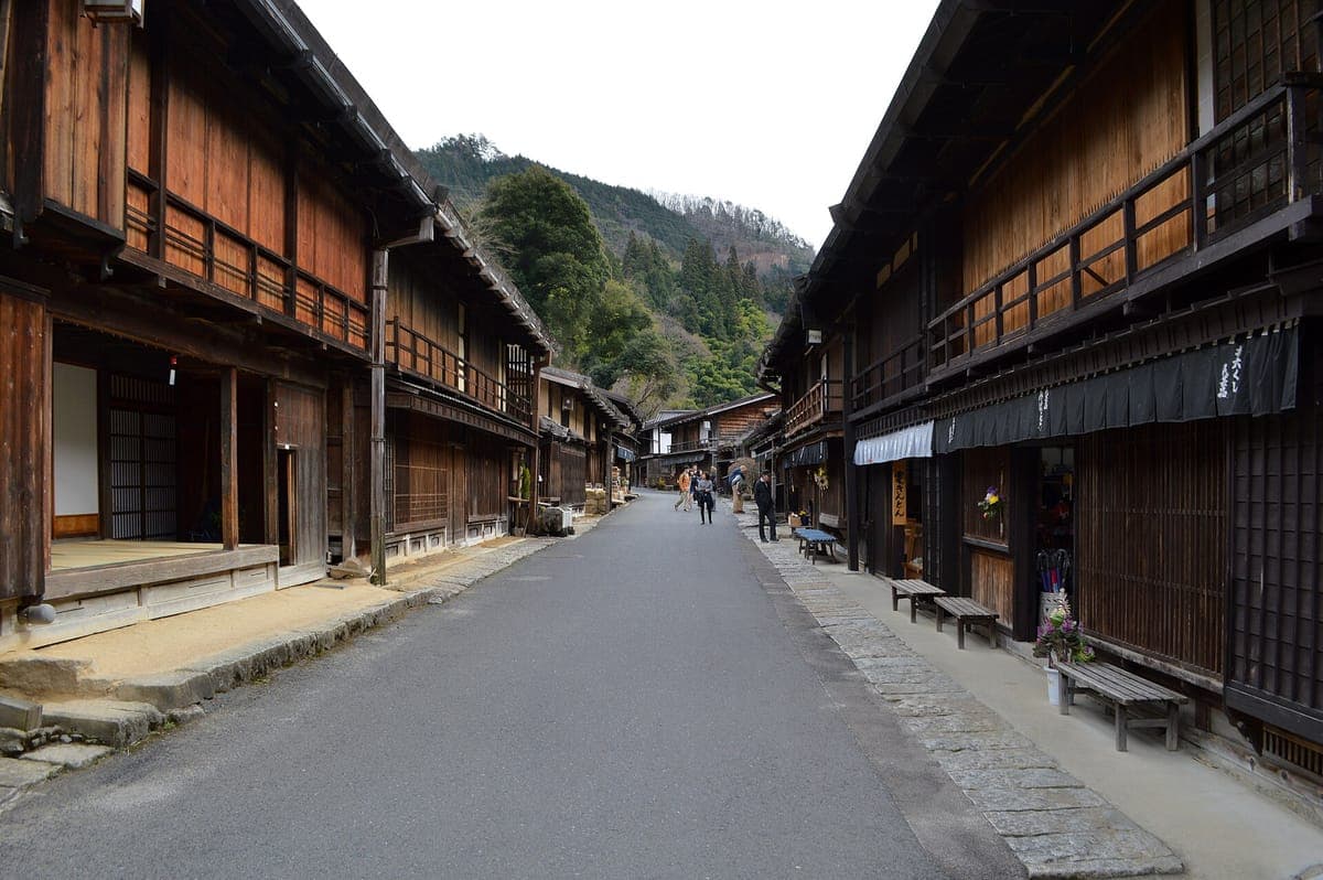 La tranquila calle principal de Tsumago-juku está bordeada a ambos lados por oscuras casas de madera de dos pisos con frentes enrejados, que conducen hacia colinas boscosas.
