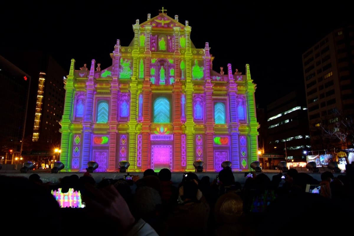 ประติมากรรมหิมะขนาดใหญ่บริเวณด้านหน้าโบสถ์สว่างไสวด้วยแสงสีชมพู เขียว และม่วงที่สดใสในตอนกลางคืน โดยมีฝูงชนที่มืดมิดเฝ้าดูอยู่ข้างหน้า
