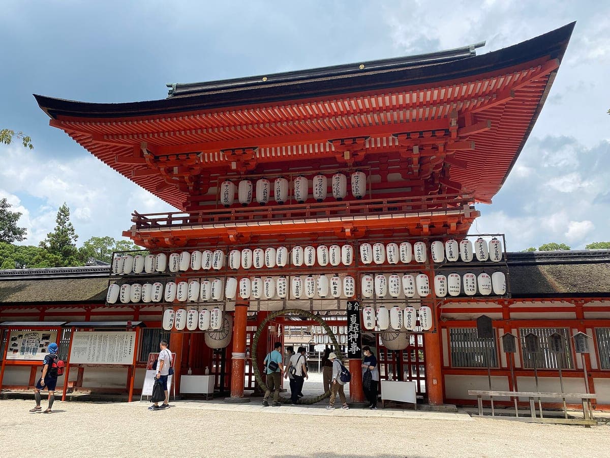 La puerta bermellón de dos pisos Rōmon de Shimogamo Jinja con un techo amplio e hileras de linternas blancas colgadas en su frente, con visitantes en la grava en frente