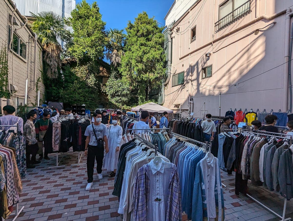 Ang mga rack ng mga second-hand na kamiseta at jacket ay nakalagay sa isang naka-tile na simento sa Shimokitazawa, kung saan ang mga mamimili ay nagba-browse sa ilalim ng mga puno at mababang gusali