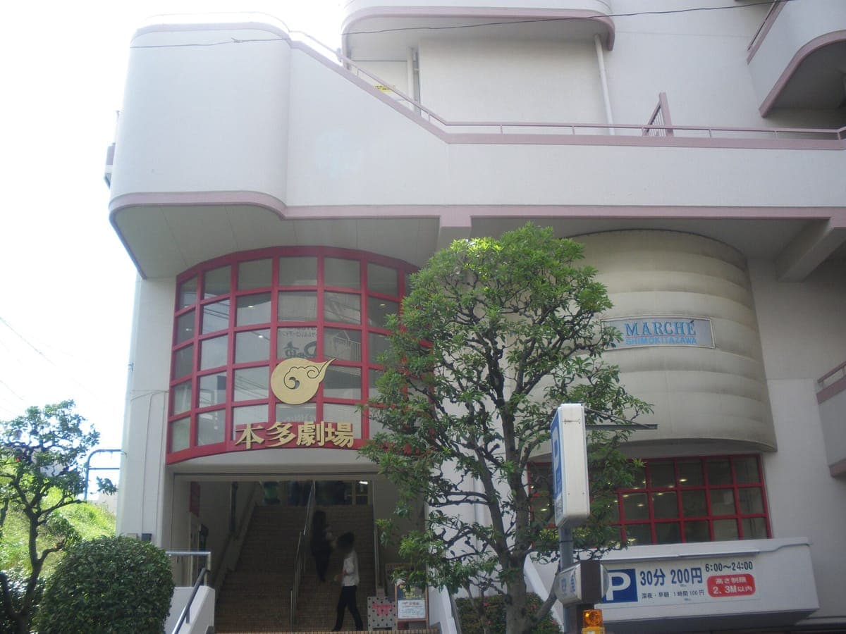 Ang pasukan ng Honda Theater sa Shimokitazawa, isang krema na gusali na may nakakurbadong bintana na may pulang frame at ang pangalan ng teatro sa pulang kanji sa itaas ng mga pinto