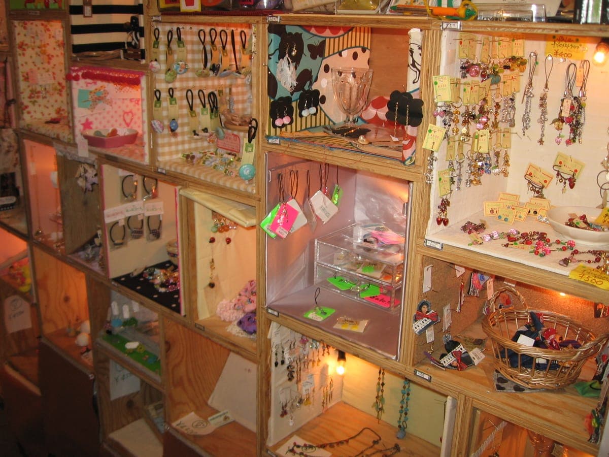 Mga hilera ng maliliit na kahon ng display na gawa sa kahoy sa isang Shimokitazawa na tindahan, bawat isa ay puno ng mga handmade na accessories, key ring, hikaw at maliliit na crafts