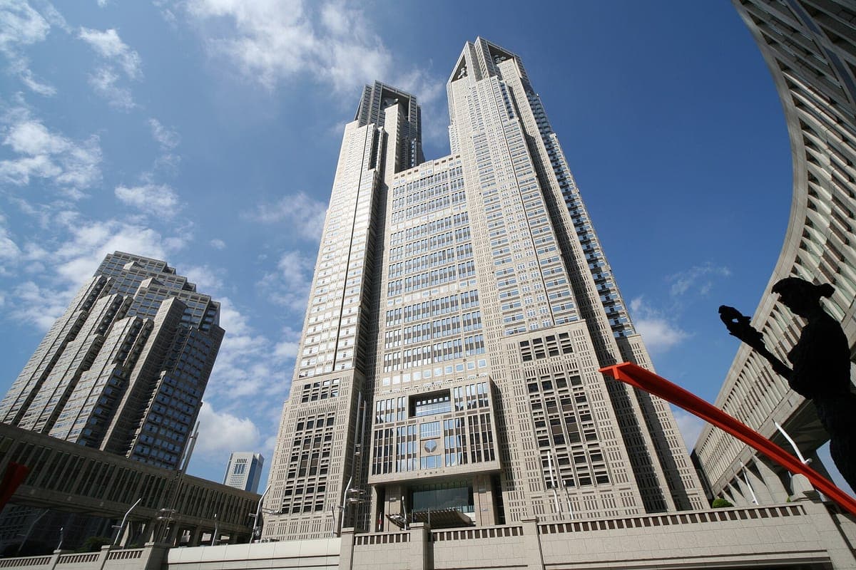 El edificio del Gobierno Metropolitano de Tokio, de dos torres, en Shinjuku, visto desde abajo contra un cielo azul con nubes blancas