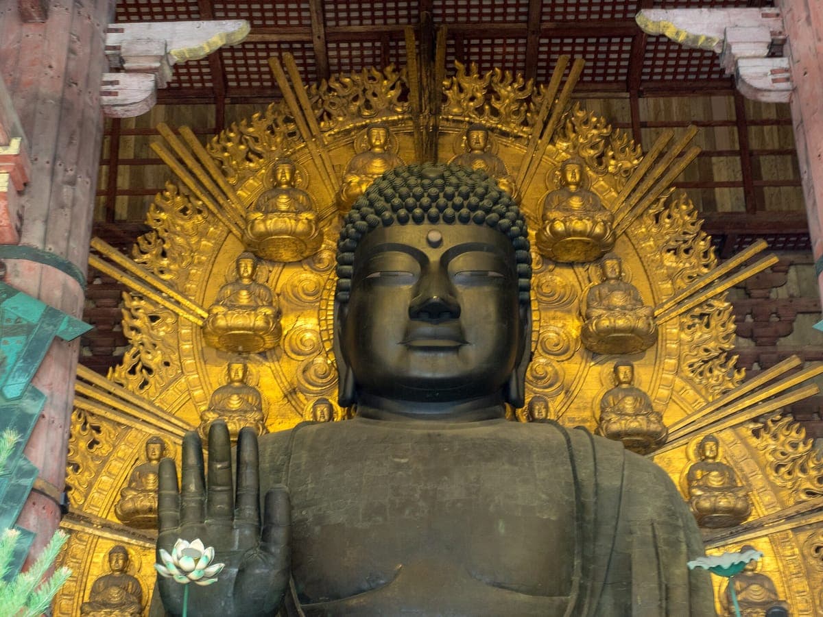 Tōdai-ji's Suuren Buddhan tummat pronssiset kasvot ja kohotettu oikea käsi kultaisen halon edessä, joka on koristeltu pienillä Buddha-hahmoilla