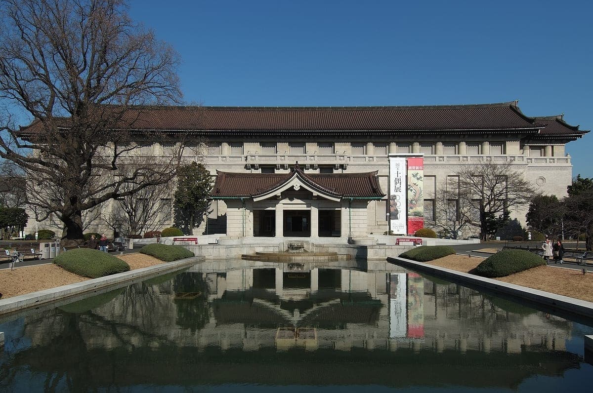 The long symmetrical Honkan of the Tokyo National Museum with its tiled Japanese roof, reflected in a rectangular pond under a blue sky