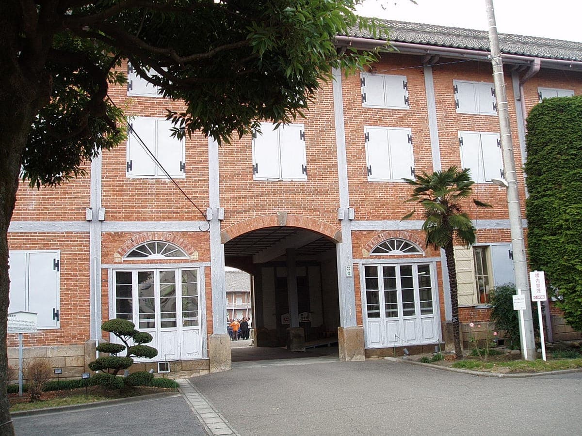 Gudang Kepompong Timur yang terbuat dari batu bata merah di Pabrik Sutra Tomioka, dengan jendela tertutup berwarna putih, atap genteng, dan lorong tengah melengkung yang diapit oleh pintu putih