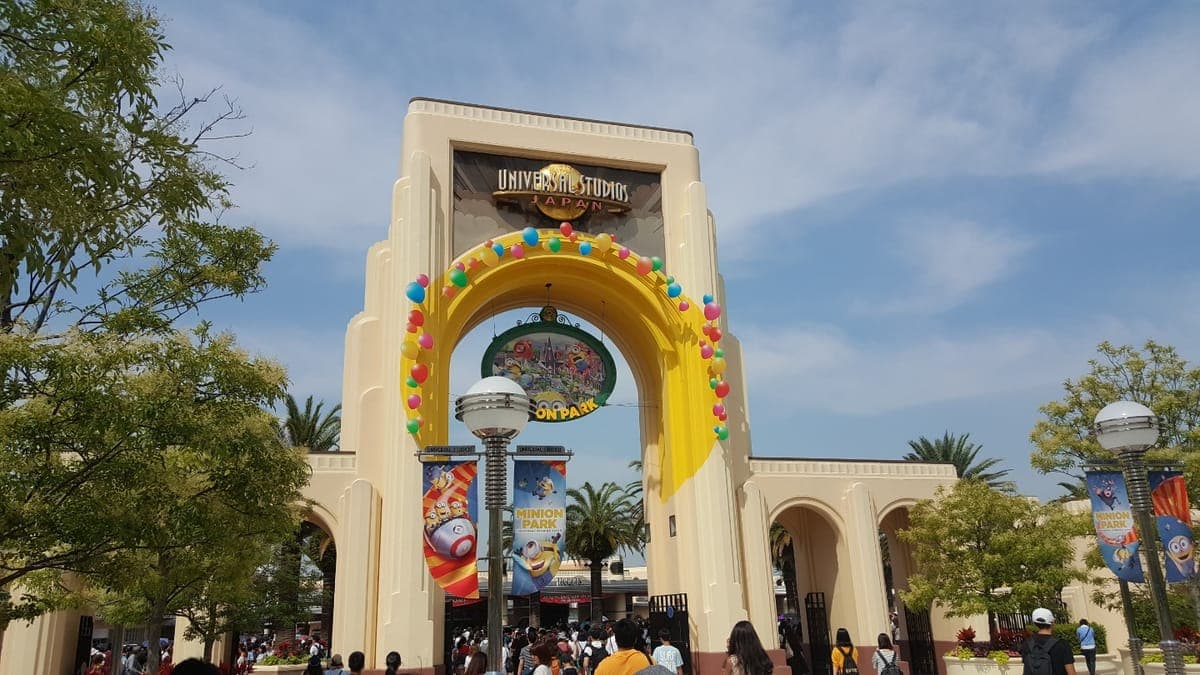 Ang kulay cream na entrance arch ng Universal Studios Japan na pinalamutian ng makulay na singsing, na may mga palm tree at mga bisita sa harapan