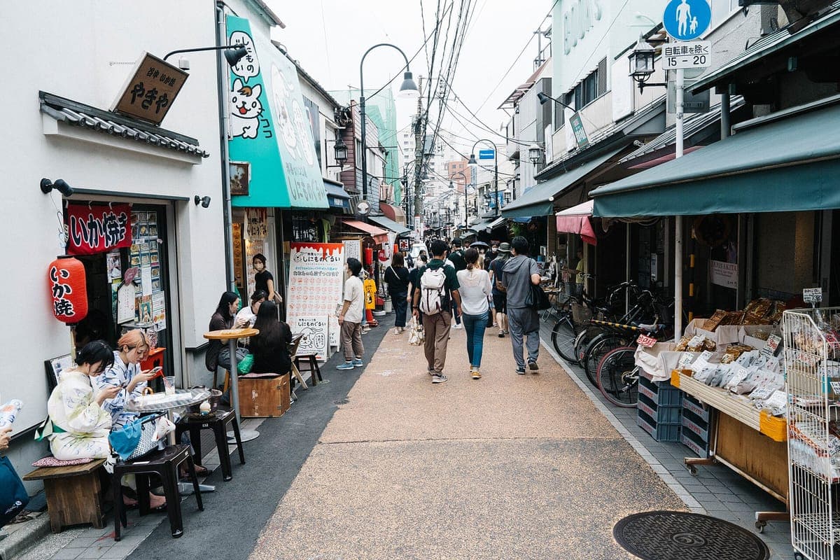 Úzká Yanaka Ginza nákupní ulice s malými výlohami, visícími lucernami, markýzami, nápisem ve tvaru kočky a nakupujícími procházejícími mezi stánky