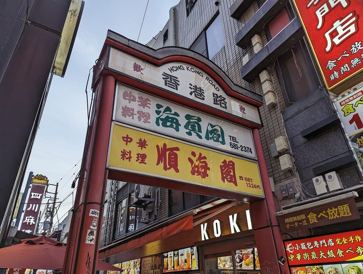 Róg ulicy w Yokohama Chinatown z czerwono-białym szyldem bramy Hongkong Road i wysokimi szyldami restauracji z chińskimi znakami