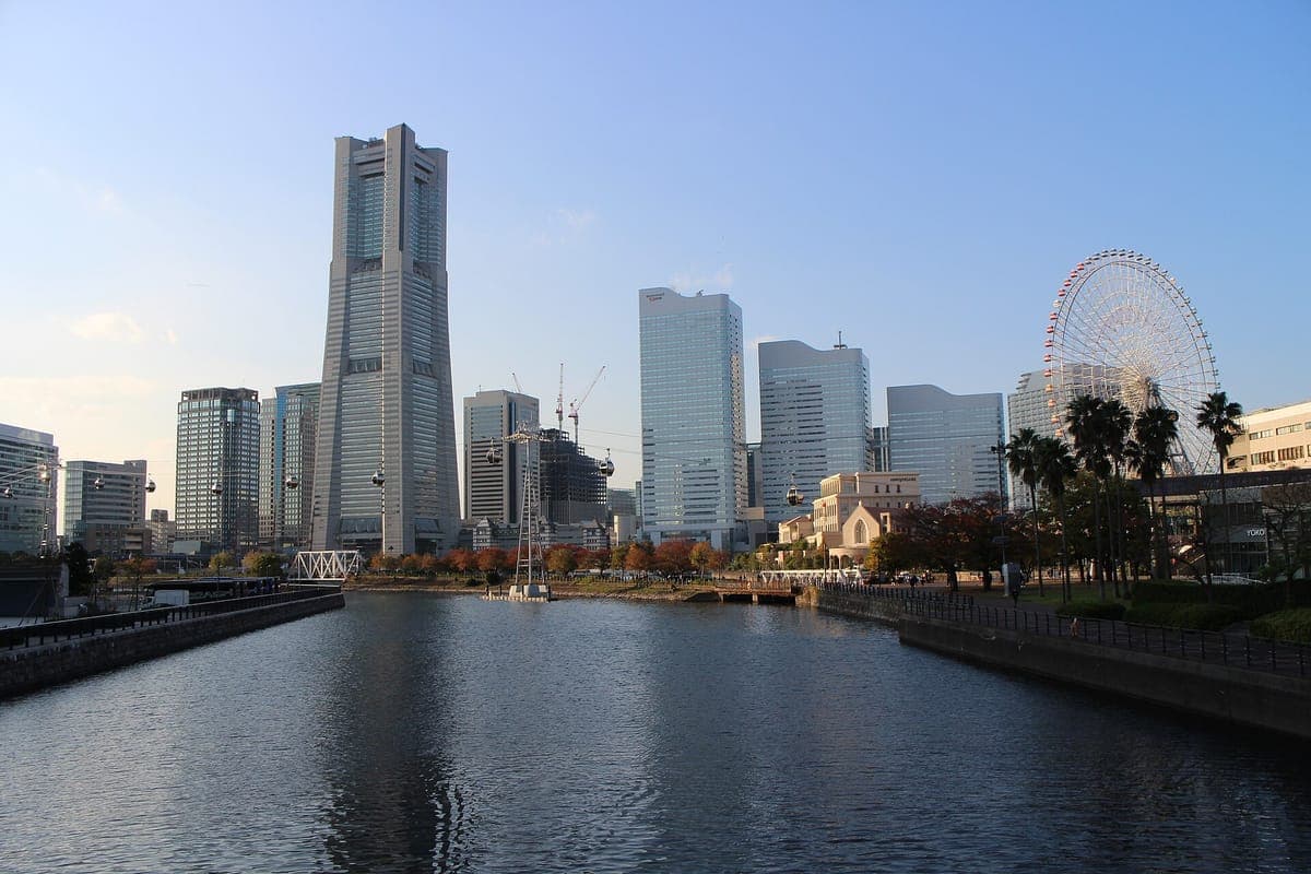 El horizonte Minato Mirai en Yokohama con la alta Landmark Tower, una hilera de torres de oficinas y una gran noria a la derecha, reflejada en un tranquilo canal