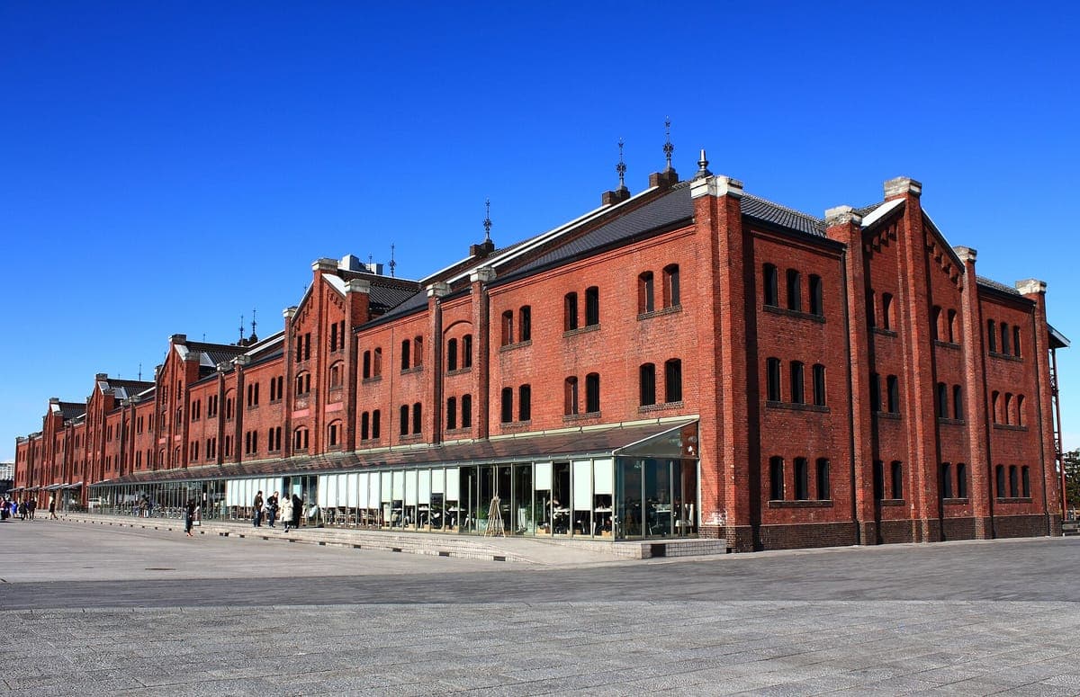 La larga fachada de ladrillo rojo de un edificio de Yokohama Red Brick Warehouse con ventanas arqueadas y balcones de hierro, bajo un cielo azul claro