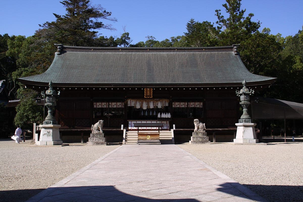 Die große hölzerne Andachtshalle von Izanagi Jingū auf der Insel Awaji mit breitem Ziegeldach, Steinlaternen und schützenden Löwenhundstatuen auf einem Kieshof