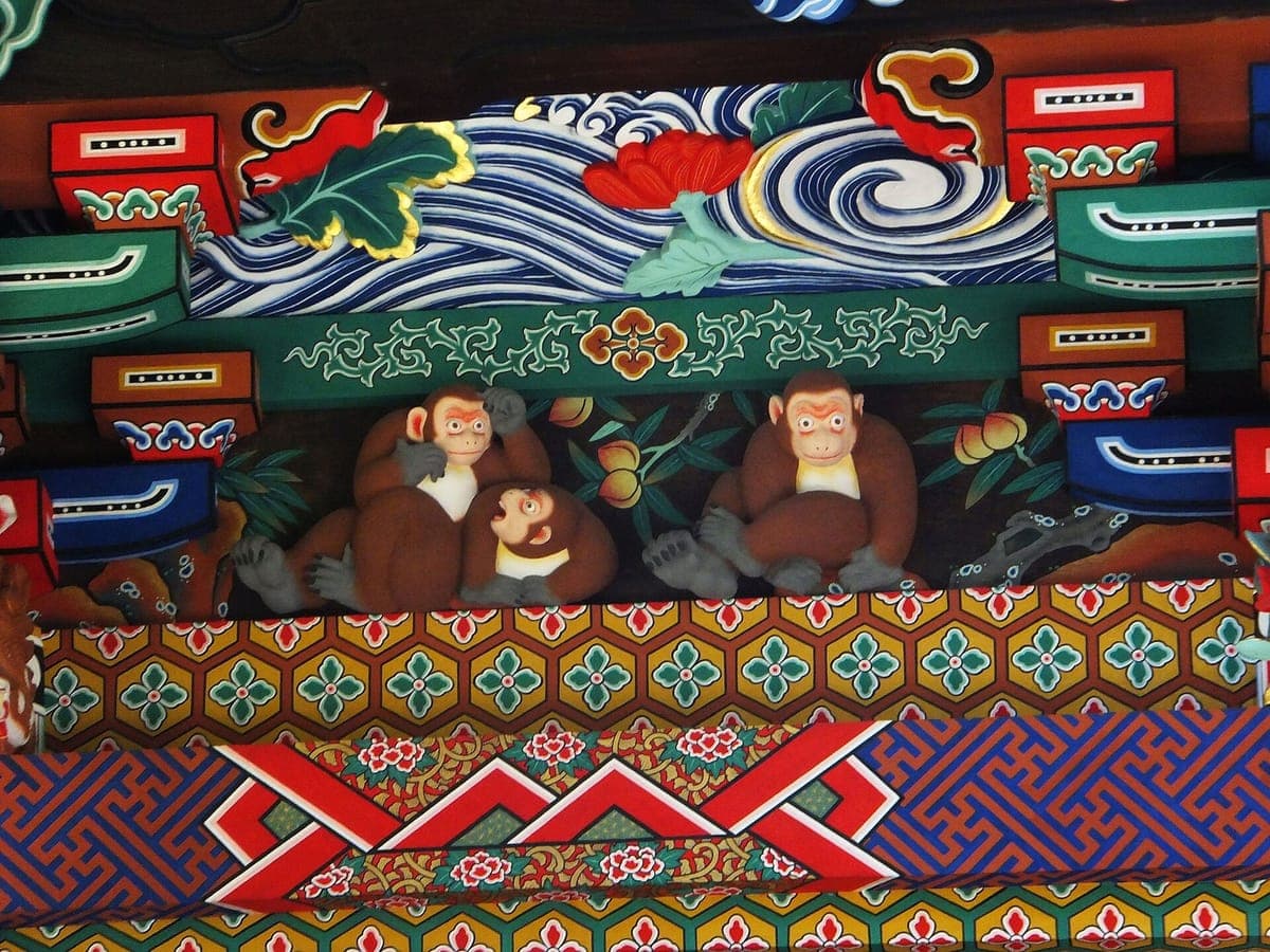 Brightly painted wooden carving on Chichibu Shrine showing three monkeys among leaves, beneath blue and white waves and red and green bracket decoration