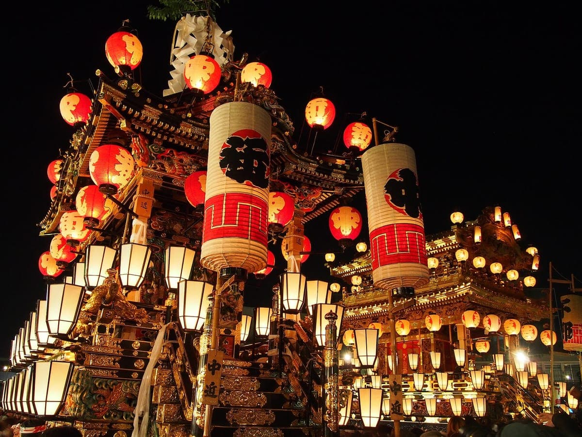 An ornate festival float of the Chichibu Night Festival at night, hung with rows of glowing red and white paper lanterns and gilded carvings