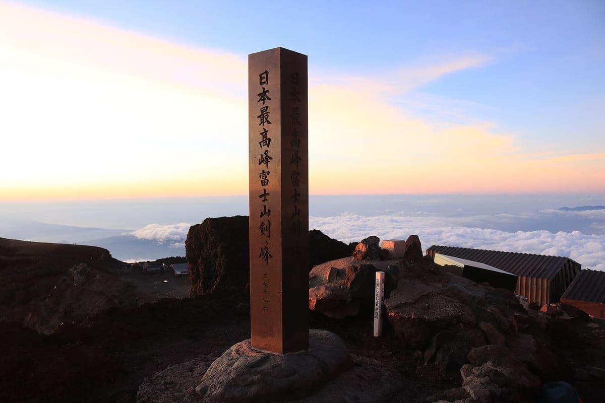 De hoge stenen marker bij Kengamine, het hoogste punt van de berg Fuji, tegen een bleke ochtendhemel met wolken ver beneden