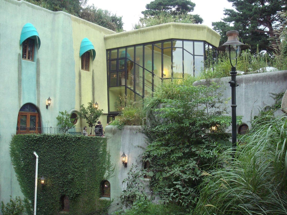Las paredes de color verde pálido y crema del Museo Ghibli con ventanas redondas, toldos verde azulado, una escalera de cristal, hiedra y plantas que crecen en las terrazas.