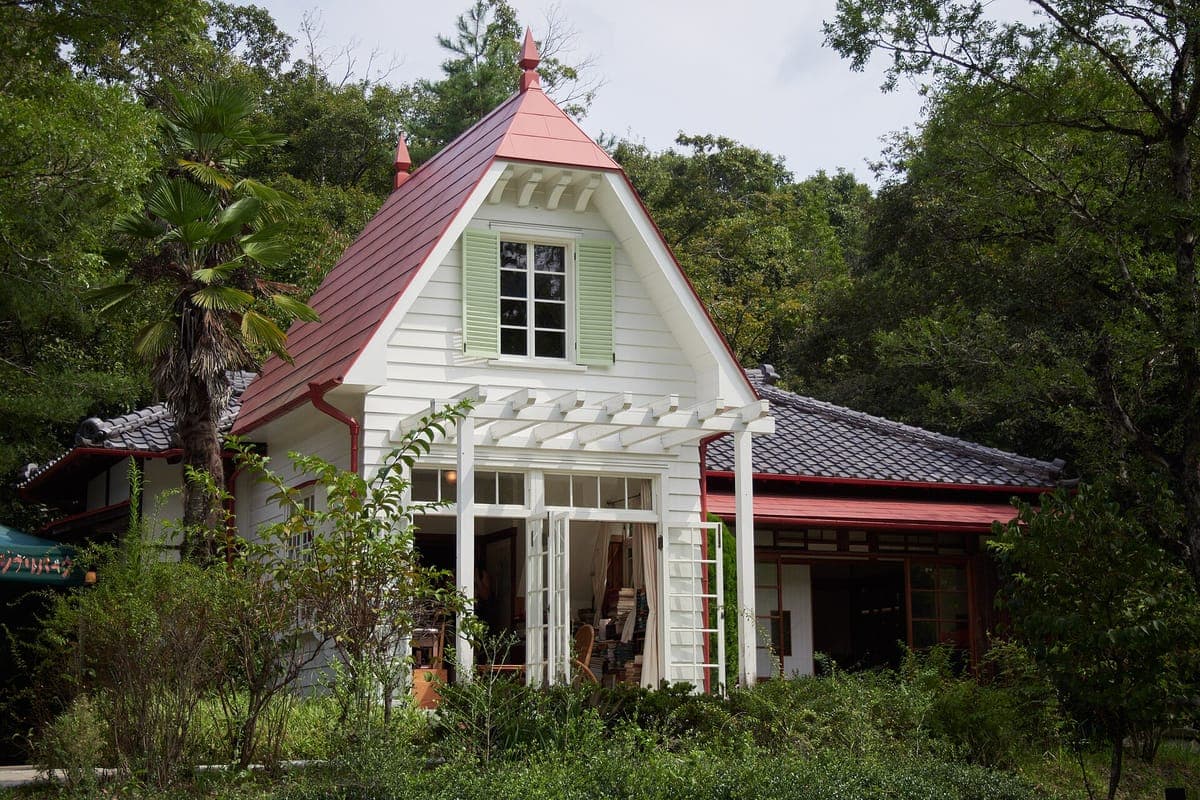 Dalawang palapag na Japanese house na may puting Western-style na pader, pulang bubong at pergola, na napapalibutan ng mga puno at halaman sa tag-init sa Ghibli Park