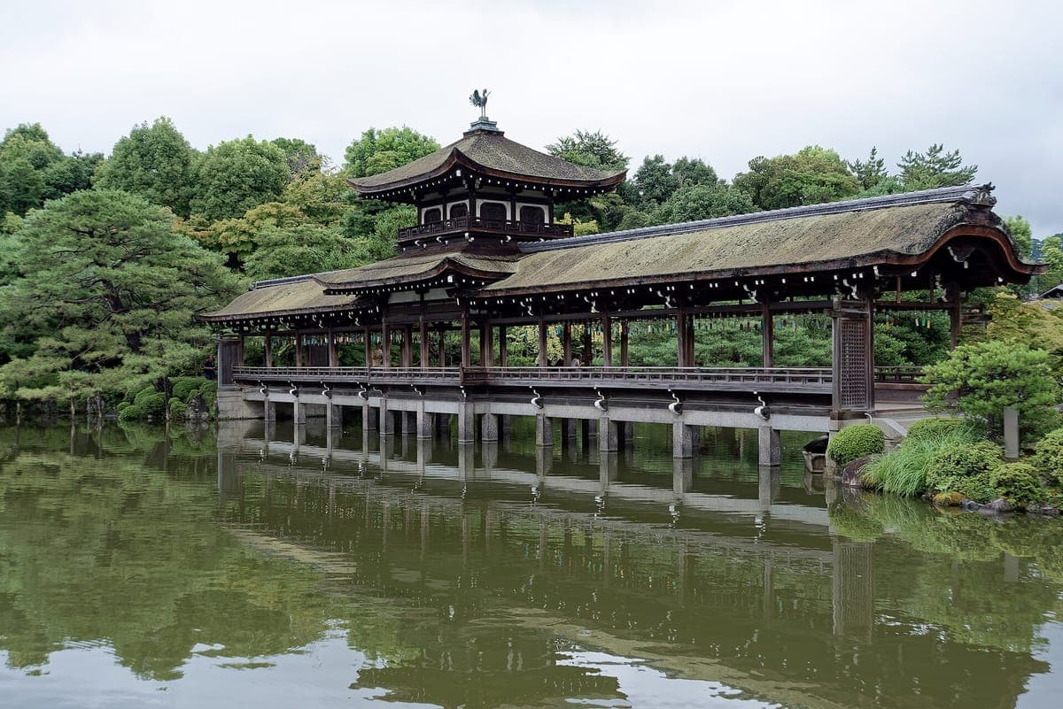 平安 Jingū's 东花园,一座长木廊桥,亭台倒映在碧绿的池塘里,周围环绕着松树
