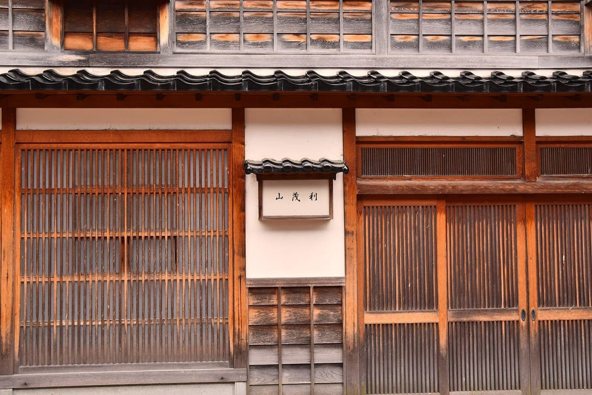 Nahansicht einer Teehausfassade in Higashi Chaya mit feinem vertikalen Holzgitter, einem kleinen weißen Namensschild und Schiebetüren